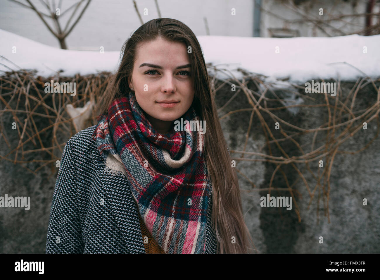 Portrait junge Frau in karierten Schal gegen Schnee bedeckte Wand Stockfoto