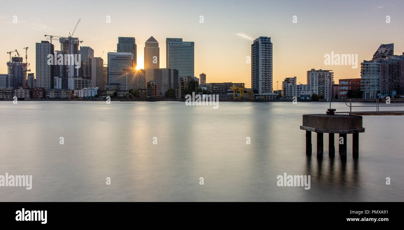 London, England, Großbritannien - 2 September, 2018: Die Sonne hinter einem Cluster von Wolkenkratzern in den Londoner Docklands Canary Wharf Nachbarschaft, mit dem Fluss Stockfoto