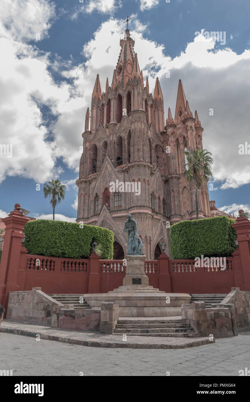 Parroquia de San Miguel Arcángel, Statue von Fray Juan de San Miguel im Vordergrund, viel Grün und dramatischen Blau bewölkter Himmel, in San Miguel de Allende Stockfoto