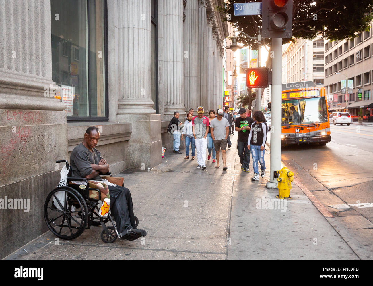 Downtown Los Angeles Szene, Mann im Rollstuhl, wenige Fußgänger, ein Bus und ein Auto. Stockfoto
