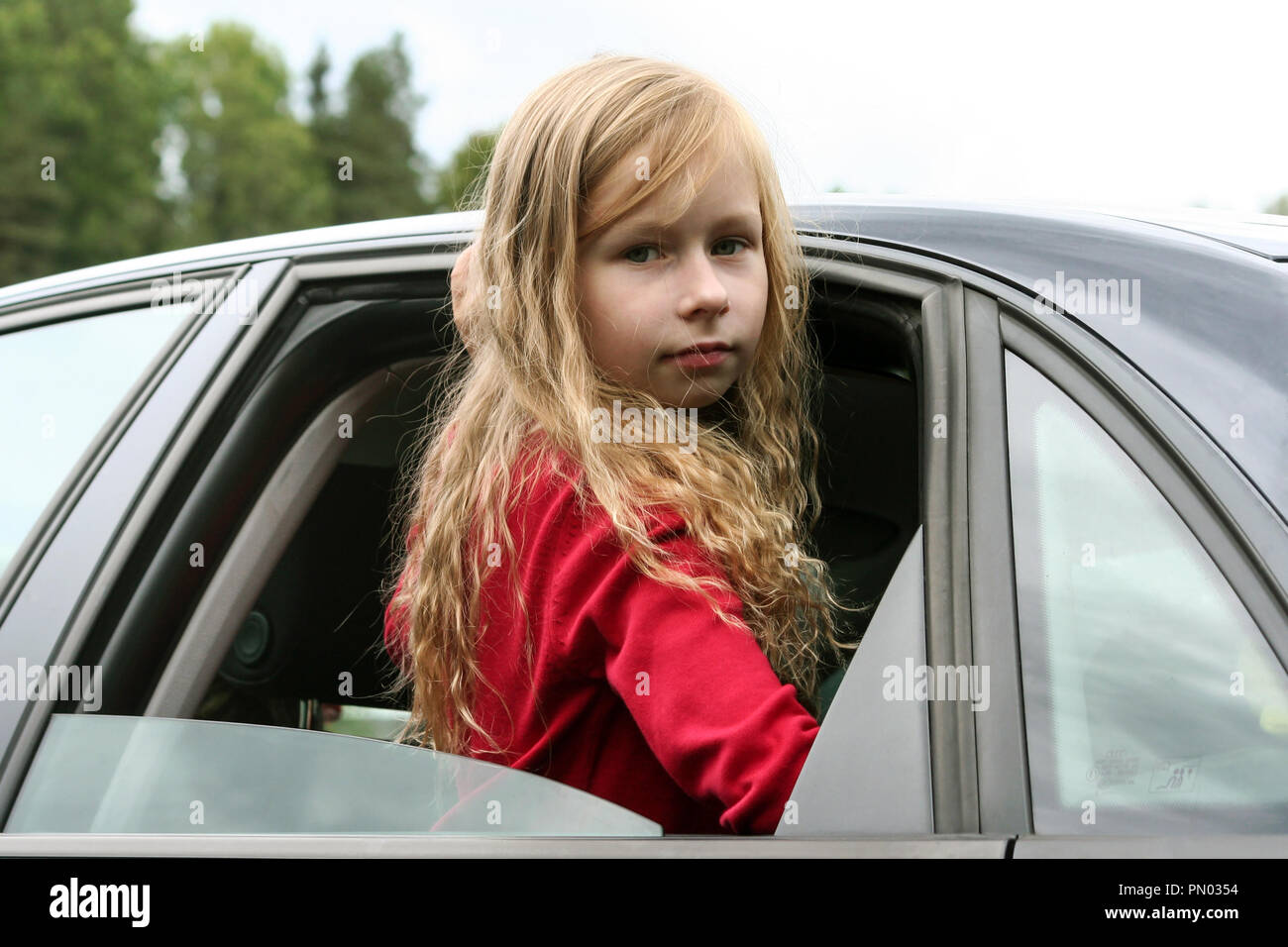 Kleines Mädchen mit langen blonden Haaren und in einer roten Jacke sieht  durch das offene Fenster des Autos in die Kamera, kletterte aus dem  Fenster, um die Taille Stockfotografie - Alamy