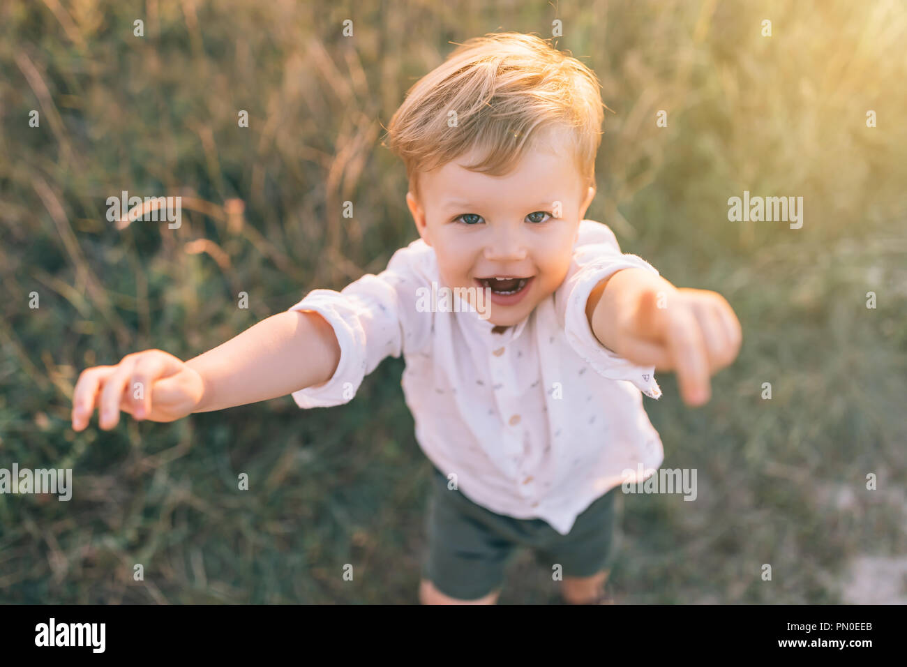 Hohe Betrachtungswinkel von Adorable Little Boy erreichen Hände und lächelt in die Kamera im Freien Stockfoto