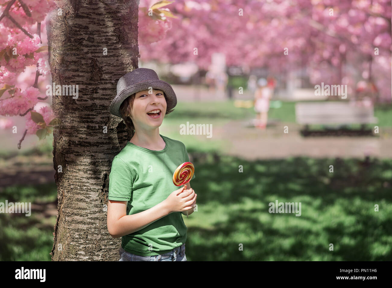 Porträt einer fröhlichen Jungen in einem T-Shirt und Hut stehen auf dem Hintergrund der blühenden Bäume. In seinen Händen ein süßes Süßigkeit. Stockfoto
