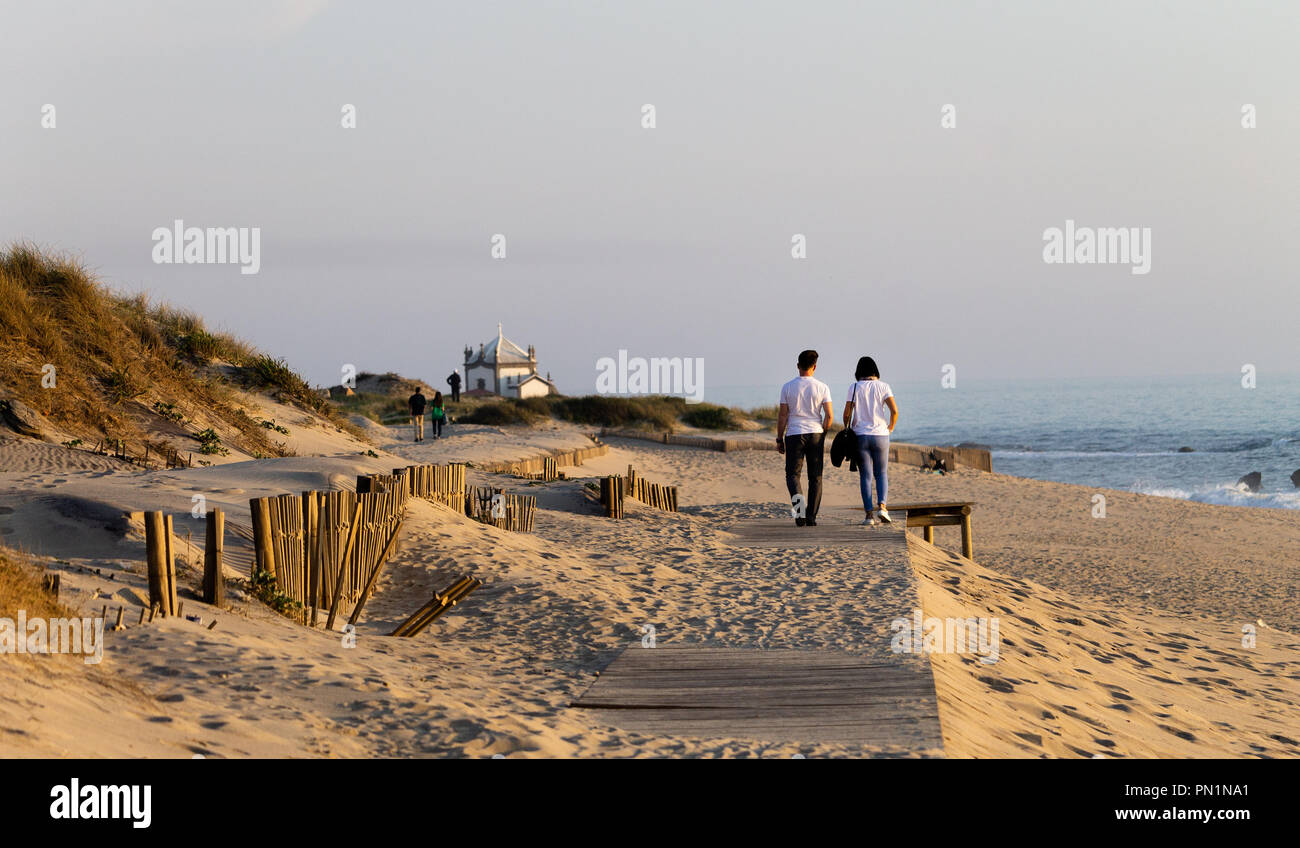 Ein junges Paar Spaziergänge entlang der Promenade in der Nähe der Küste, mit einer Kapelle im Hintergrund. Stockfoto
