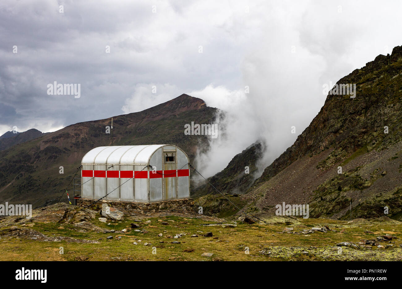 Eine kleine Hütte aus Stahl sitzt vor der Bergkette von Nebel und Dunst gefüllt vor einem Sturm. Stockfoto