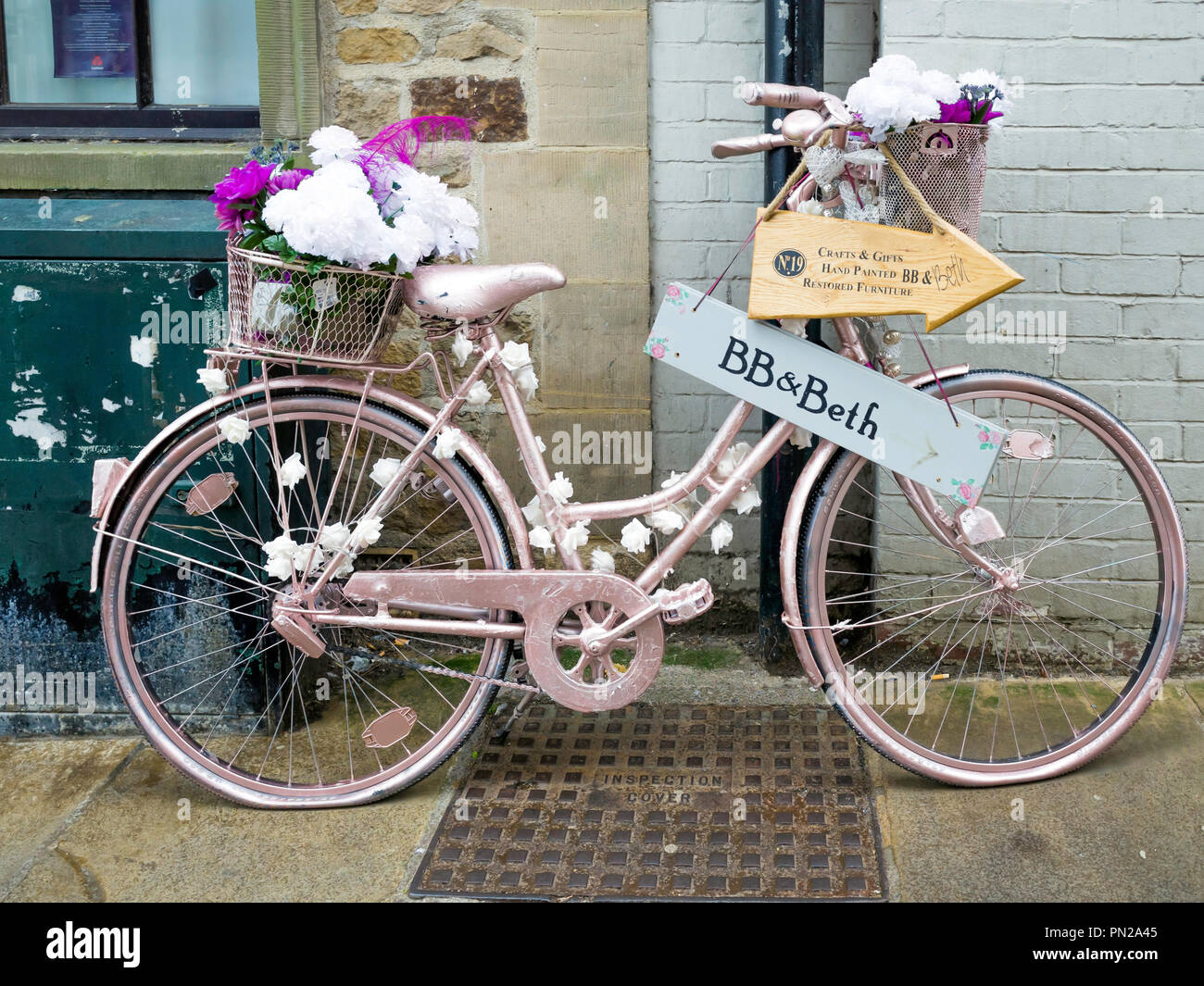 Ein Damen Fahrrad rosa lackiert und mit Blumen Werbung BB und Beth ein Möbel Restauratoren shop in Richmond, North Yorkshire eingerichtet Stockfoto