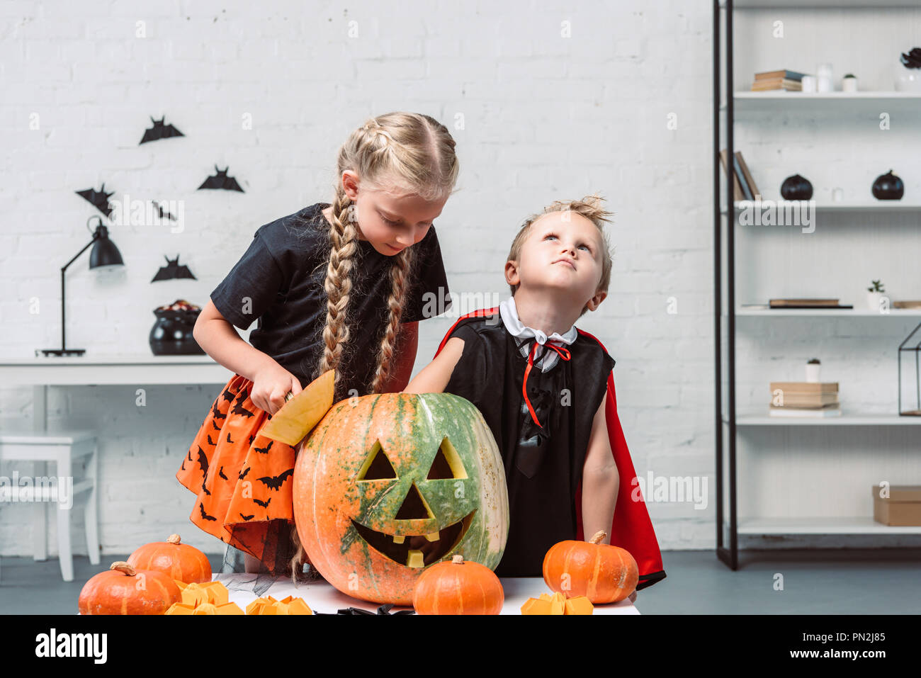 Portrait von kleinen Geschwister in Halloween Kostüme in der Nähe von  Tabelle mit Kürbissen zu Hause Stockfotografie - Alamy