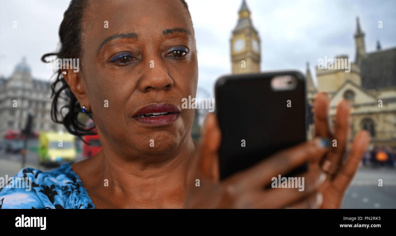 Schwarze Frau auf die London Street sieht auf Fotos von Enkelkindern auf dem Smartphone Stockfoto