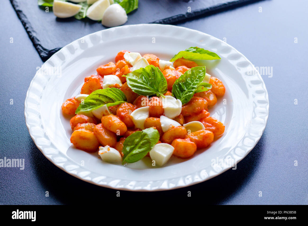 Gnocchi alla Sorrentina in Tomatensauce mit frischem Basilikum und Mozzarella Kugeln auf einem weißen Teller auf schwarzem Hintergrund serviert. Traditionelle it Stockfoto