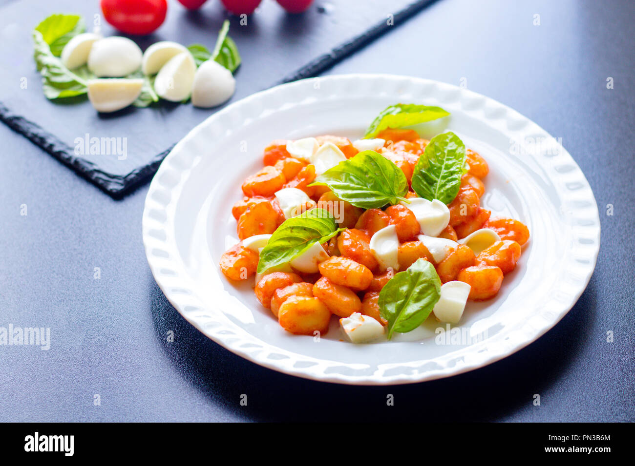 Warme italienische Gnocchi aus Kartoffeln in Tomatensauce mit frischem Basilikum und Mozzarella in Scheiben geschnittene Kugeln auf einem weißen Teller mit Zutaten aus Bl serviert. Stockfoto