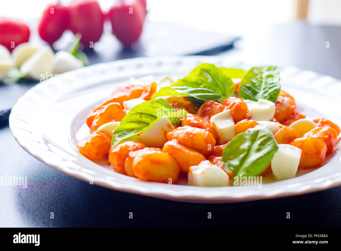 Gnocchi alla Sorrentina in Tomatensauce mit frischem Basilikum und Mozzarella Kugeln auf einem weißen Teller auf schwarzem Hintergrund serviert. Traditionelle it Stockfoto