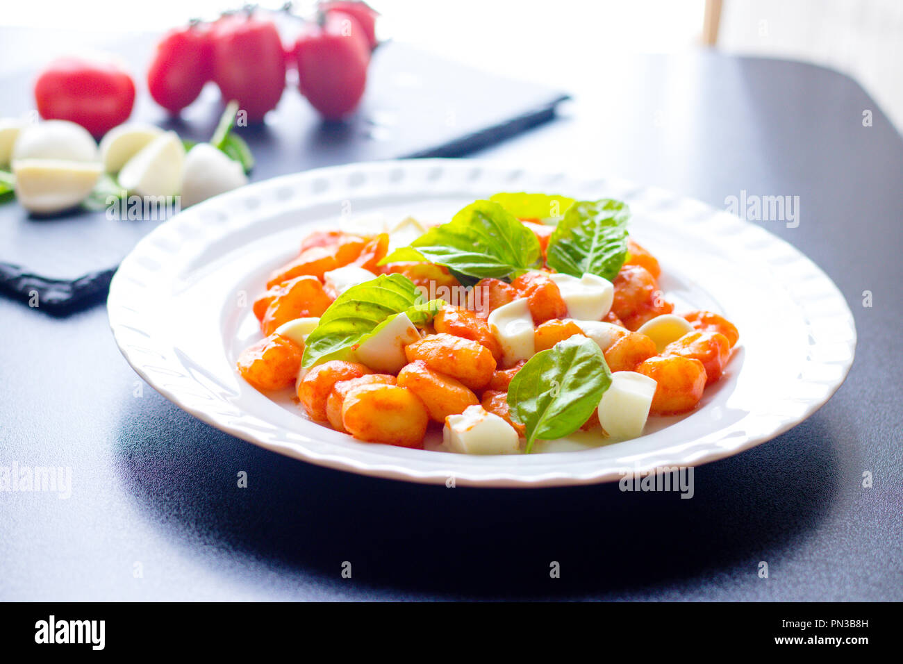 Warme italienische Gnocchi aus Kartoffeln in Tomatensauce mit frischem Basilikum und Mozzarella in Scheiben geschnittene Kugeln auf einem weißen Teller mit Zutaten aus Bl serviert. Stockfoto