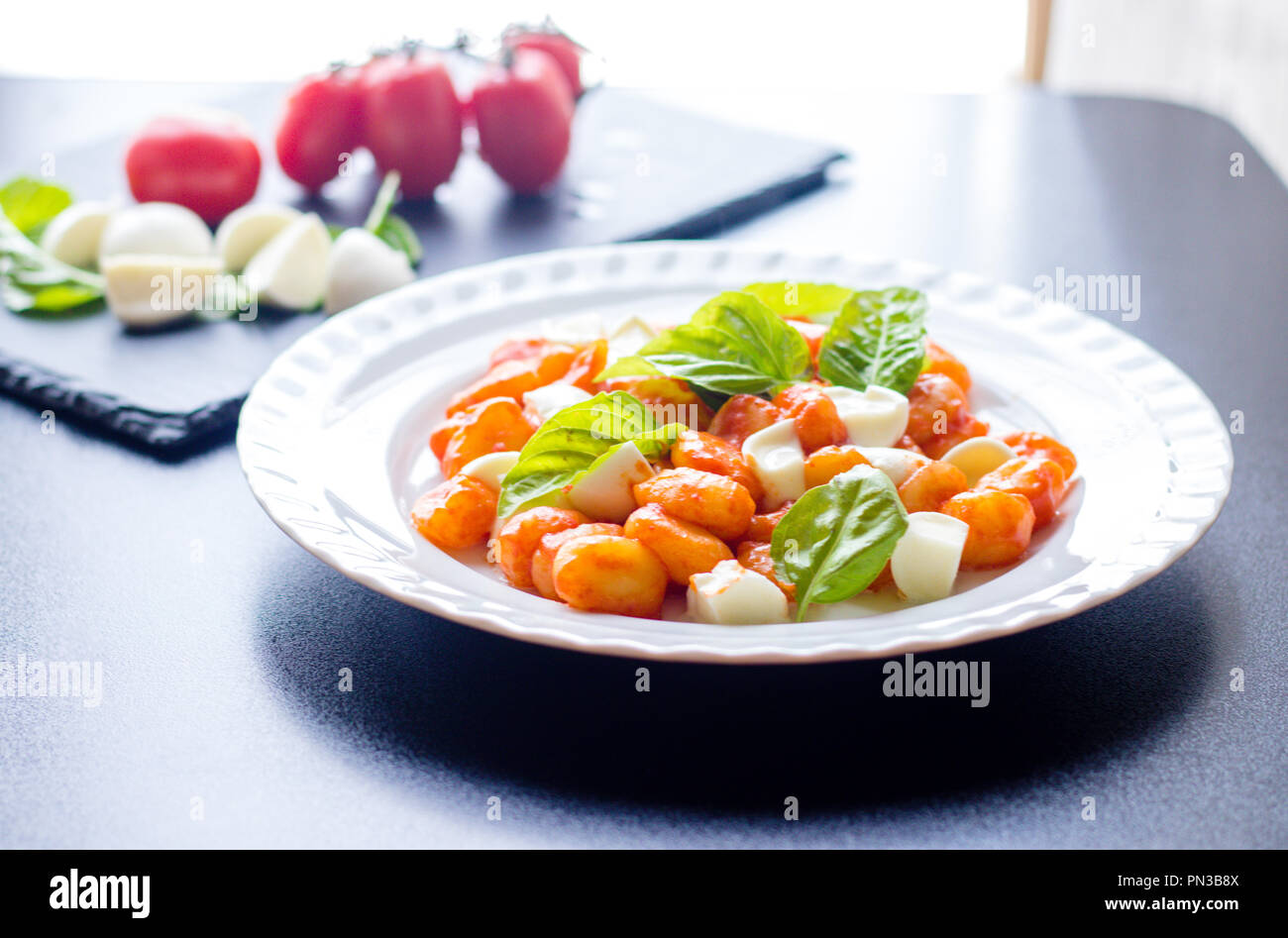 Gnocchi alla Sorrentina in Tomatensauce mit frischem Basilikum und Mozzarella in Scheiben geschnittene Kugeln auf einem weißen Teller mit Zutaten auf dem Schwarzen Brett bac serviert. Stockfoto