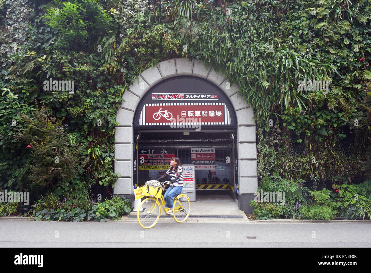 Frau reiten weg vom Fahrrad Garage mit grüne Wand, Kyoto, Japan. Keine PR oder MR. Stockfoto