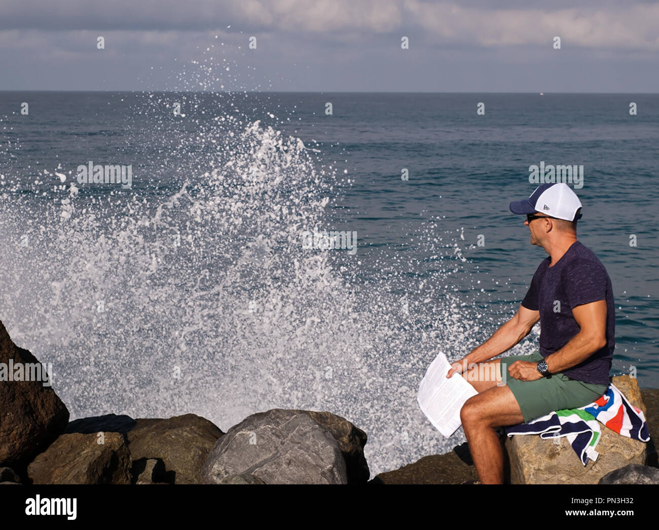 Ein Mann sitzt am Rande beobachten Wellen des Ozeans an den Felsen neben ihm aus dem Pazifischen Ozean im Süden von Kalifornien, USA Stockfoto