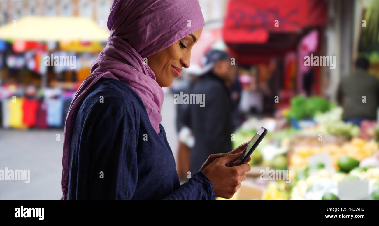 Schöne junge muslimische Frau sms mit Smartphone außerhalb Stockfoto