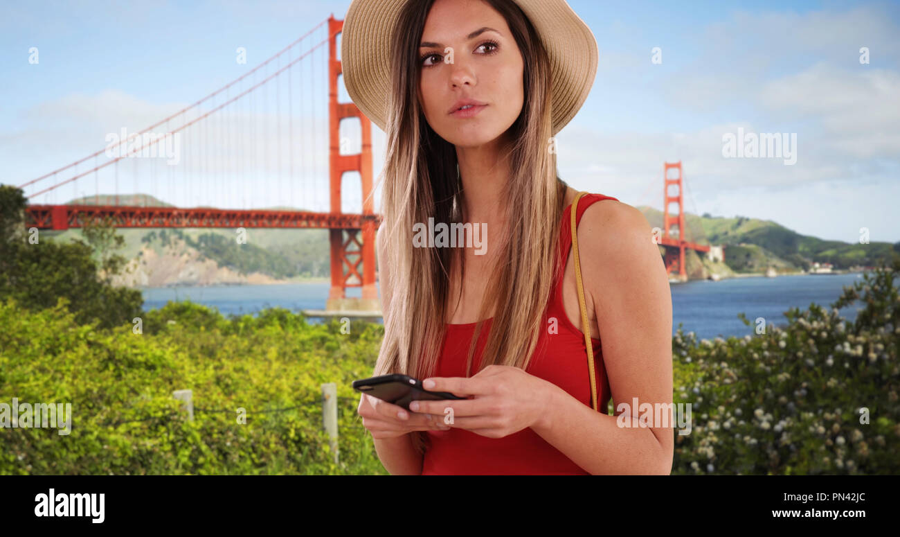 Stilvolle Frau in Rot oben mit Telefon und suchen in der Nähe von Golden Gate Bridge Stockfoto
