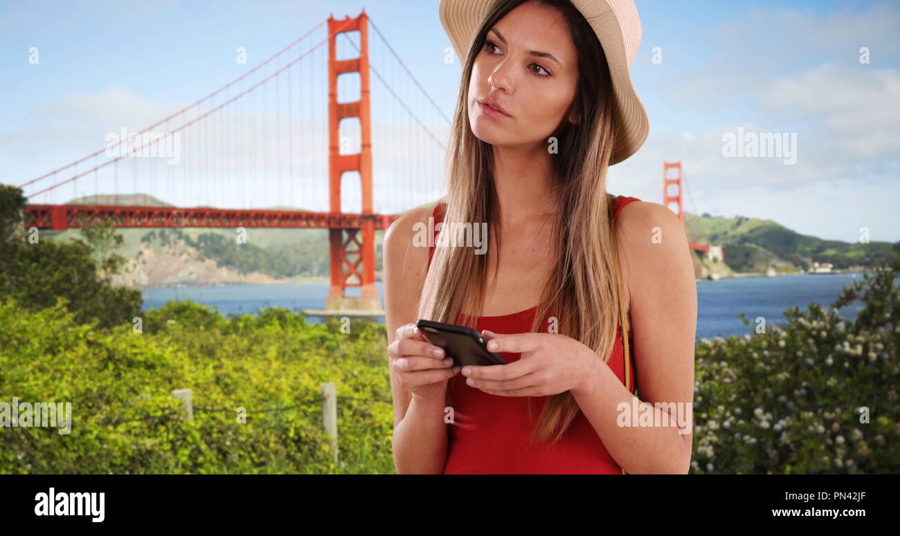Stilvolle Frau in Rot oben mit Telefon und suchen in der Nähe von Golden Gate Bridge Stockfoto