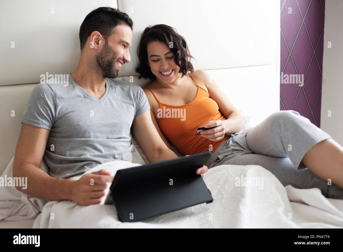 Glückliches junges Paar im Bett kaufen Reisen auf Linie Stockfoto
