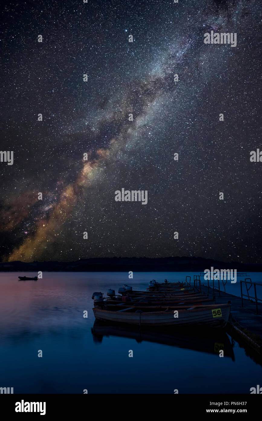 Atemberaubende leuchtende Milchstraße zusammengesetzten Bild über Landschaft noch See mit Boote am Steg Stockfoto