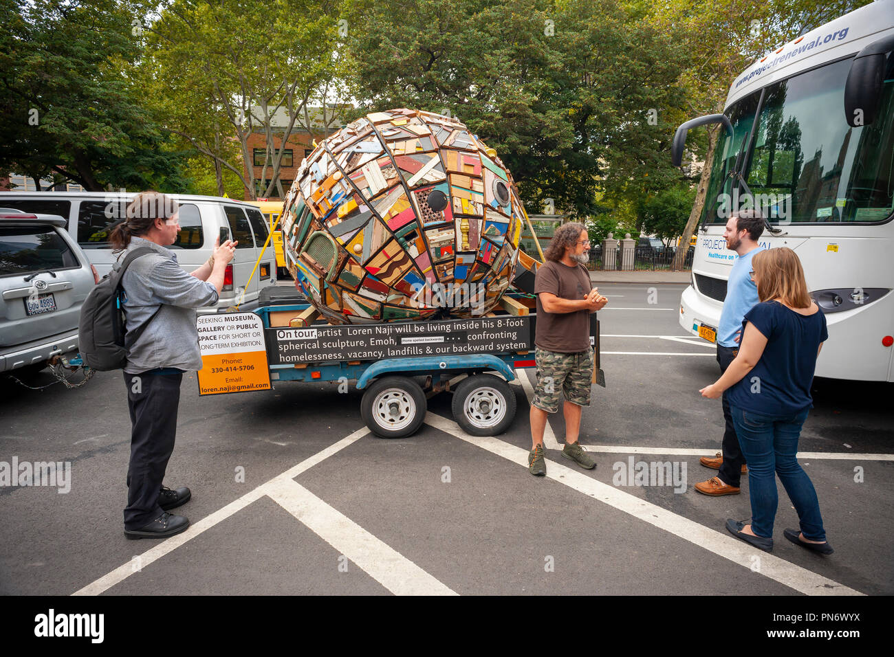 New York, USA. 20. September 2018. Cleveland Künstler Loren Naji, dritter von rechts, spricht mit neugierigen Passanten außerhalb der "Emoh" (home rückwärts buchstabiert), seinem 8-Fuß-Durchmesser Holz- sphäre blieb, vor der Kirche der Heiligen Apostel, der einen großen Suppenküche, im New Yorker Stadtteil Chelsea am Donnerstag, 20. September 2018. (Â© Credit: Richard Levine/Alamy leben Nachrichten Stockfoto