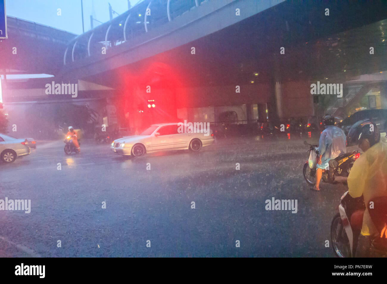 Bangkok, Thailand - 6. Juli. 2017: Menschen tragen Helm und Regenmantel fahrt Motorrad im schweren Regen durch das Wasser auf der Straße während der Regenzeit. Tr Stockfoto