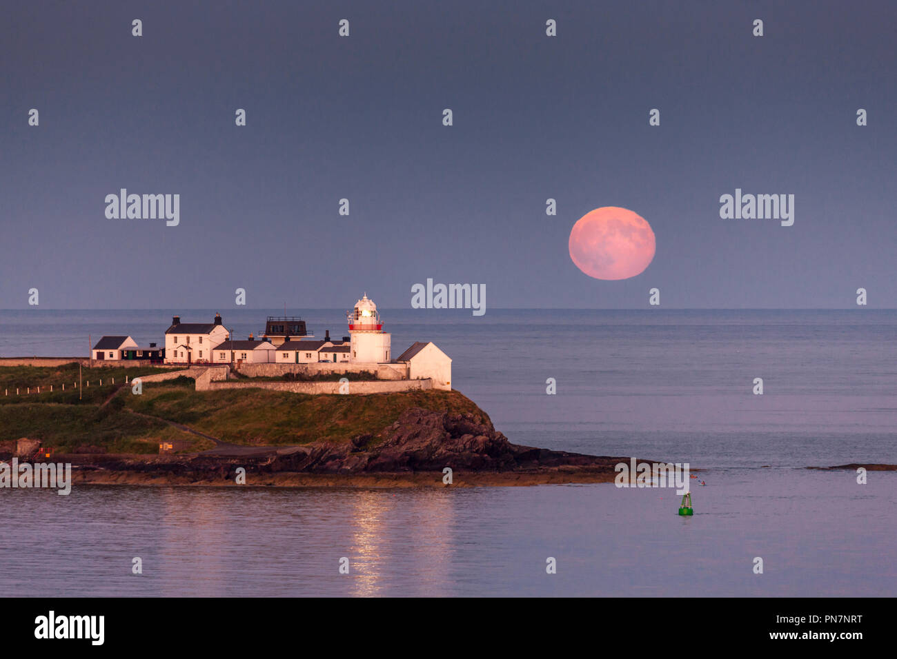 Roches Point, Irland. 28 Juni, 2018. Ein voller Mond erhebt als die letzten Sonnenstrahlen des Roches Point Leuchtturm im Hafen von Cork, Irland Leuchten Stockfoto
