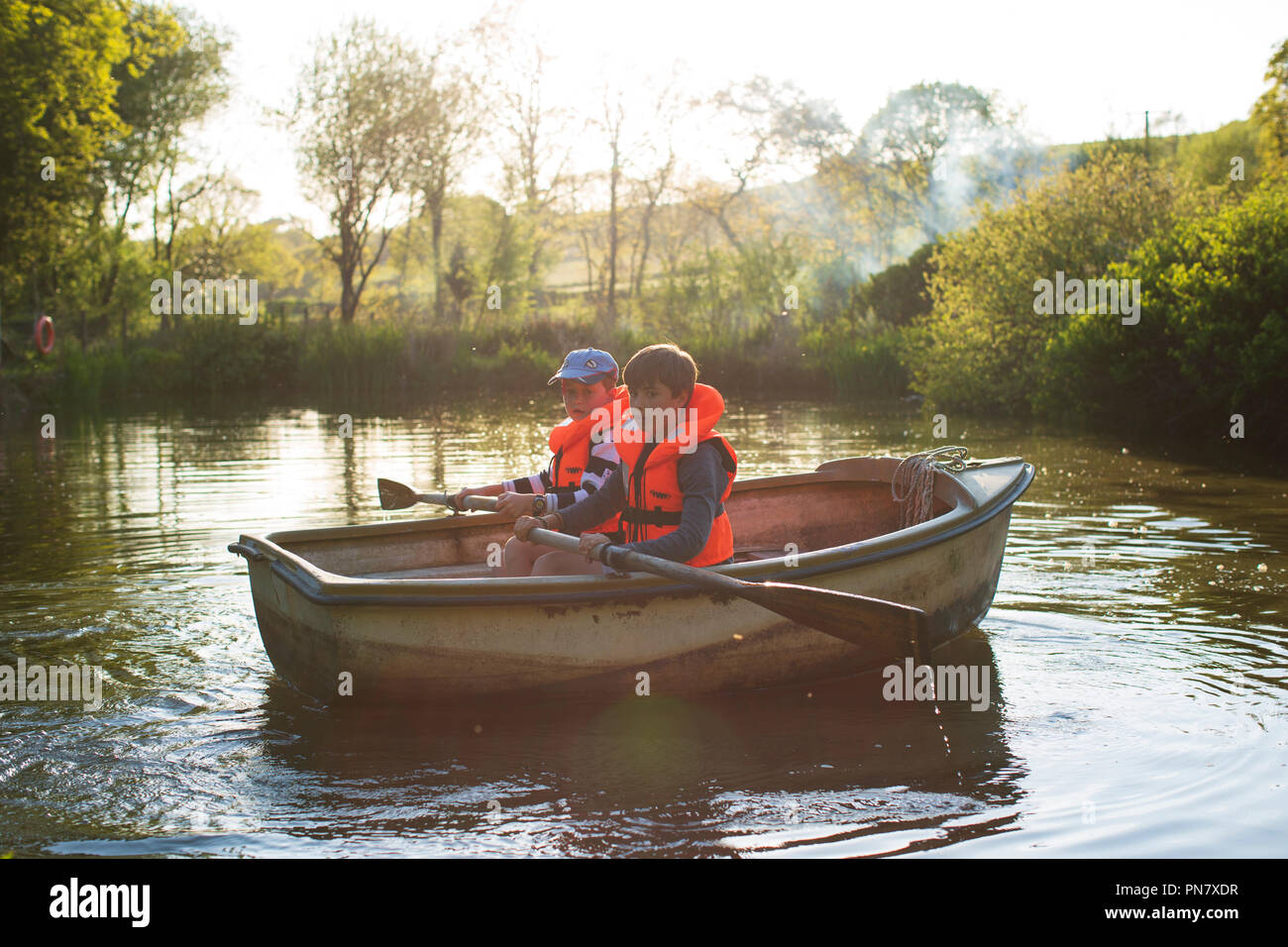 Zwei Jungen rudern ein Boot auf einem kleinen See zurück von der Abendsonne beleuchtet. Stockfoto