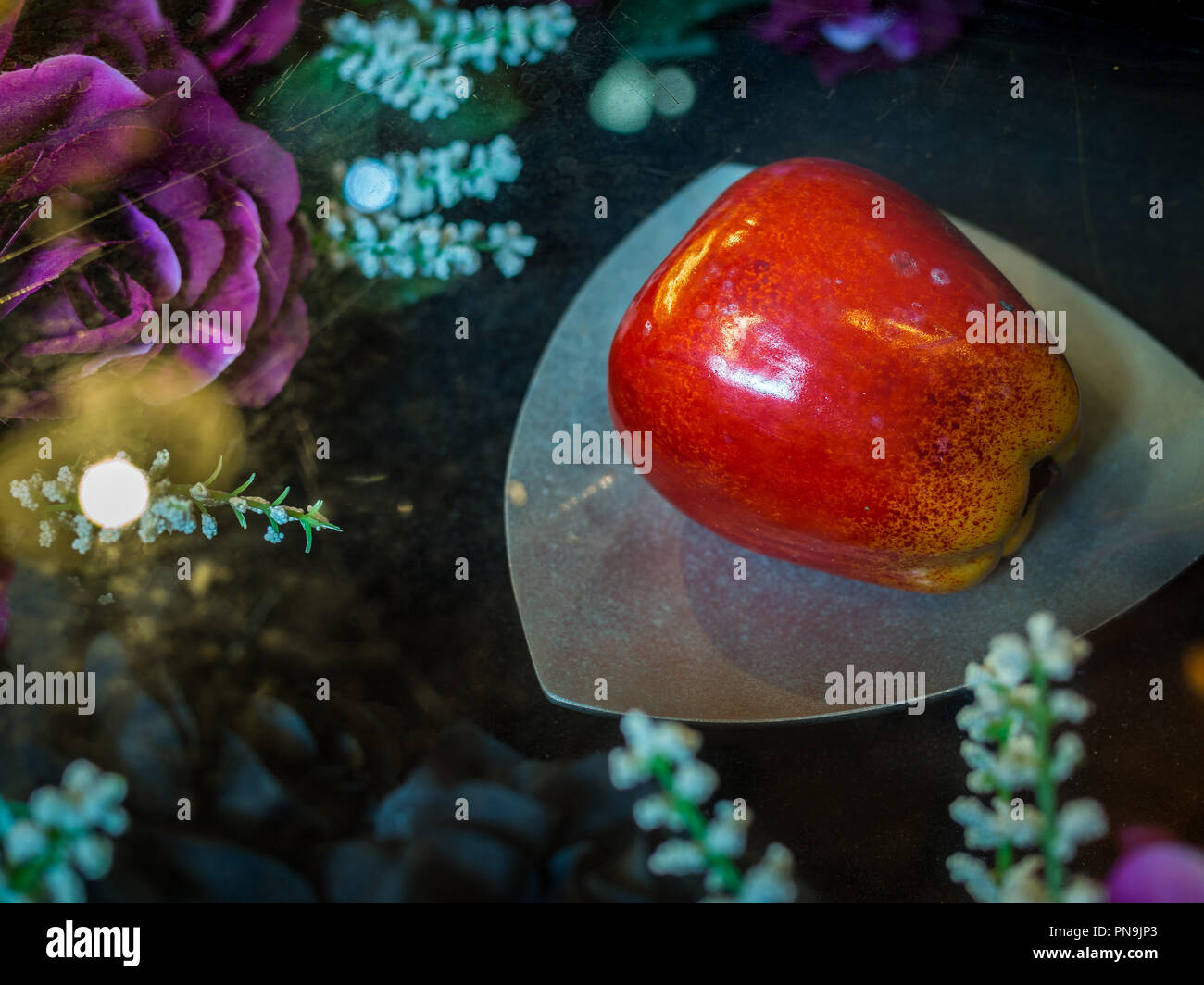 Schöne rote poison apple auf der Platte in der Nähe der roten Rosen und weißen Blüten. Stockfoto