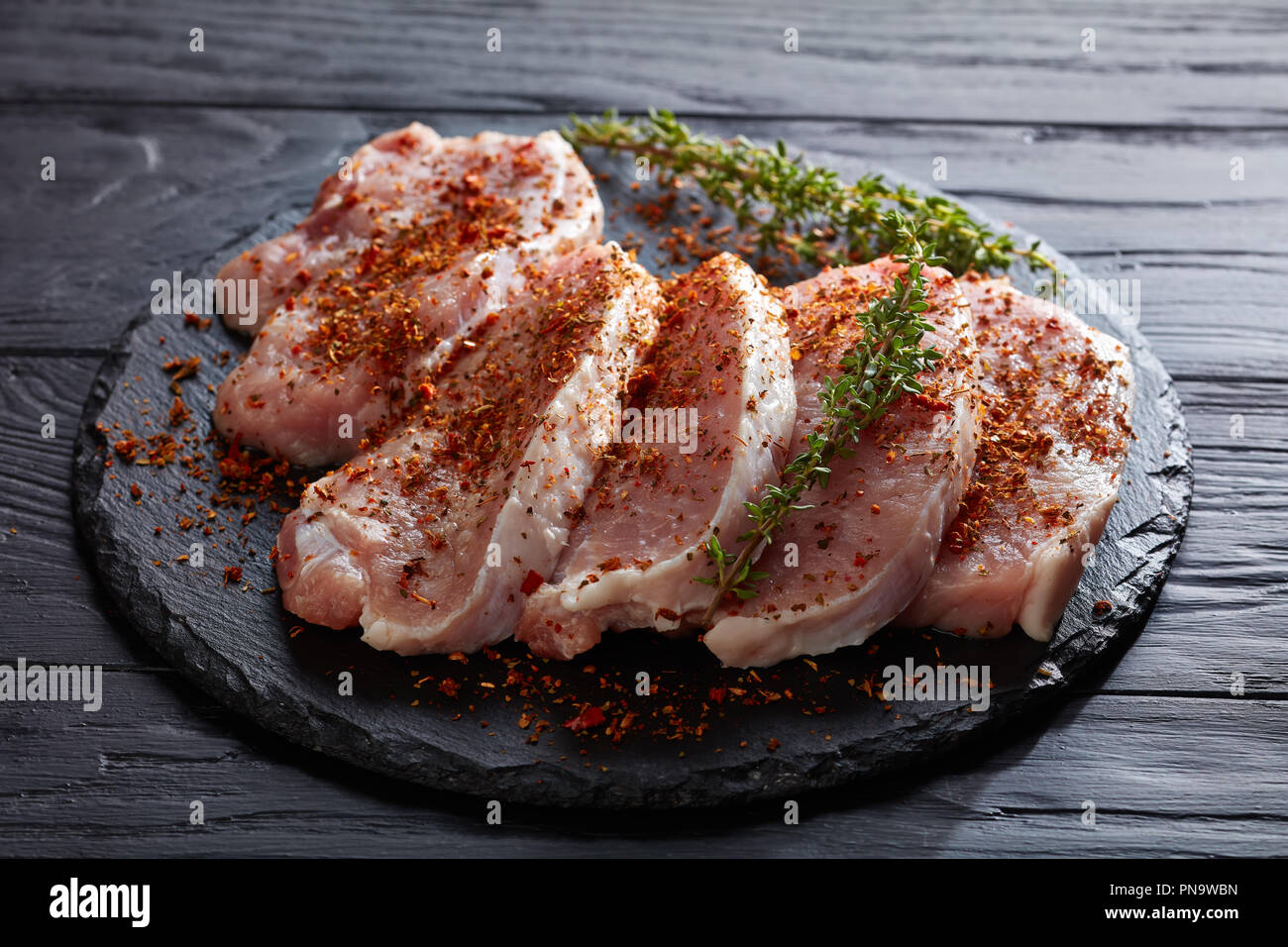 Schweinefleisch ohne Knochen schnitzel Filet gewürzt mit getrockneten Tomaten, Pfeffer, Paprika und dekoriert mit frischem Grün Thymian Stängel, auf einem runden schwarzen Stein boa Stockfoto