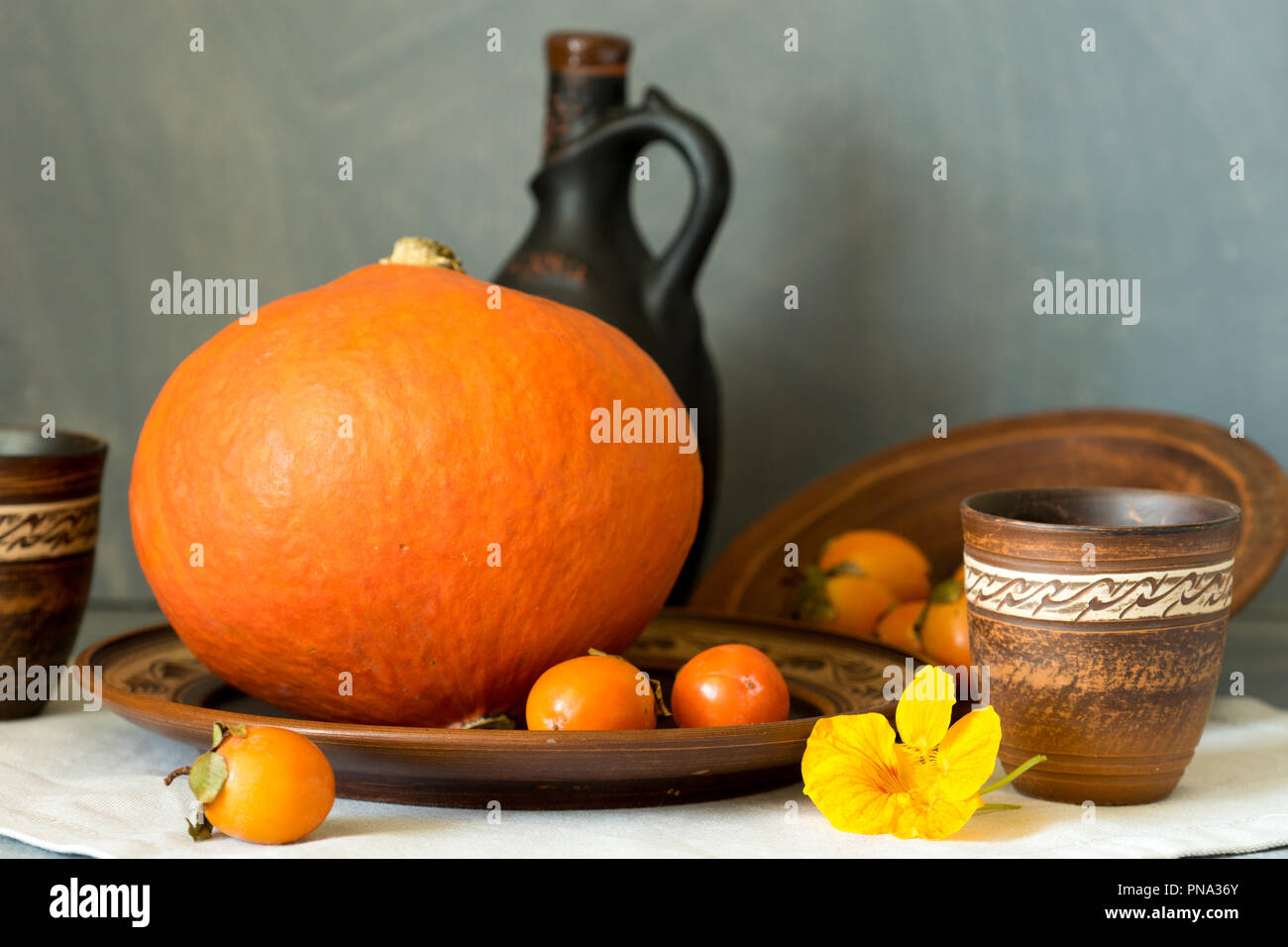 Herbst noch das Leben mit einem großen Kürbis und Persimmon in Keramik Geschirr. Stockfoto