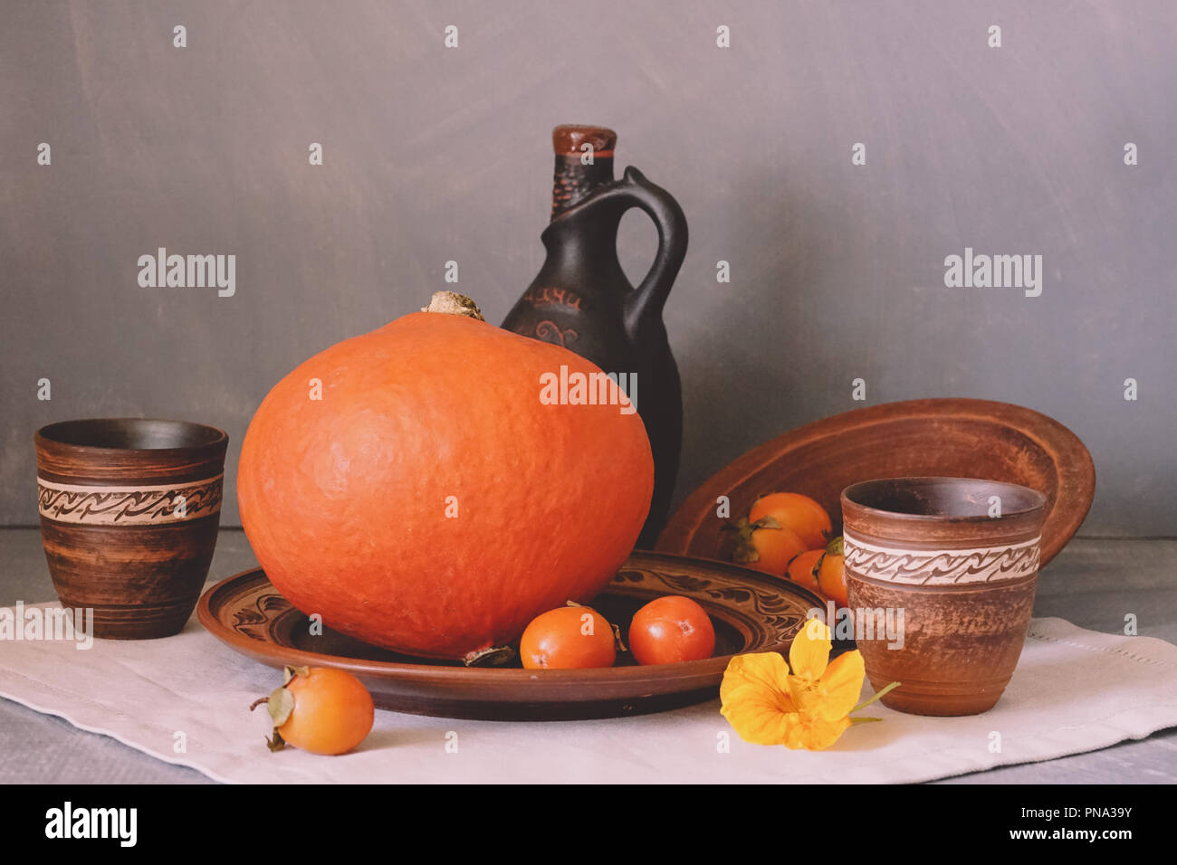 Herbst noch das Leben mit einem großen Kürbis und Persimmon in Keramik Geschirr. Stockfoto