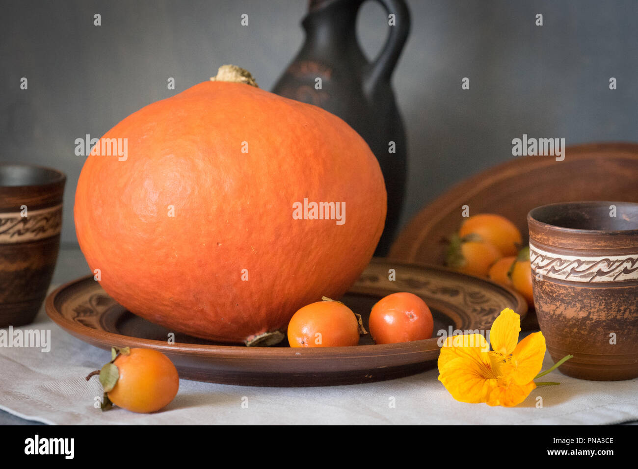 Herbst noch das Leben mit einem großen Kürbis und Persimmon in Keramik Geschirr. Stockfoto