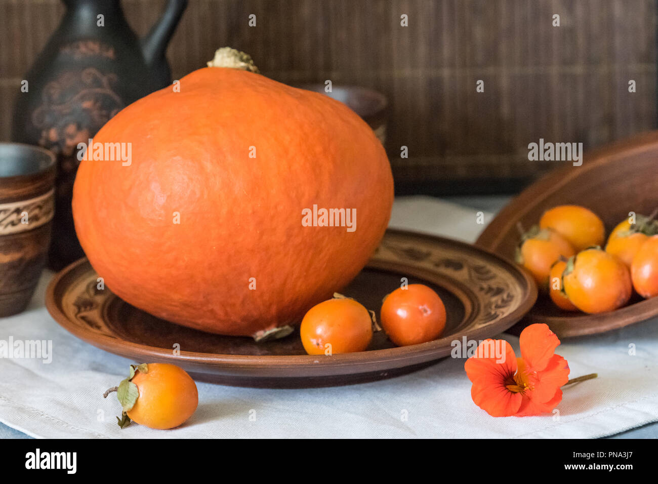 Herbst noch das Leben mit einem großen Kürbis und Persimmon in Keramik Geschirr. Stockfoto