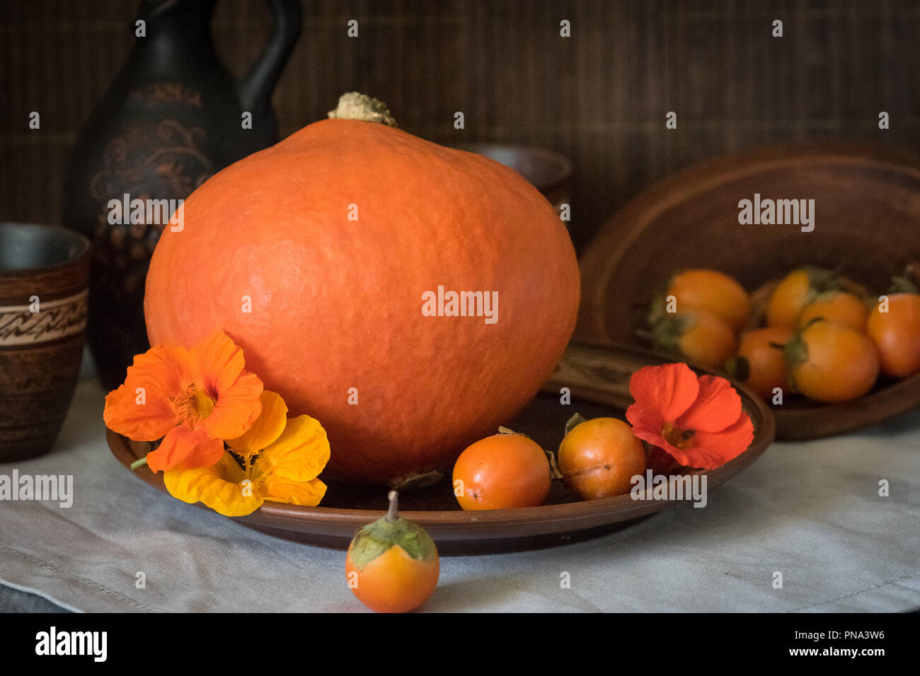 Herbst noch das Leben mit einem großen Kürbis und Persimmon in Keramik Geschirr. Stockfoto