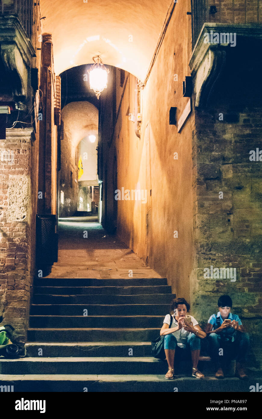 Siena, Italien - September 8, 2018: zwei Touristen mit ihren Handys in einer dunklen Gasse in der Altstadt von Siena, Italien Stockfoto
