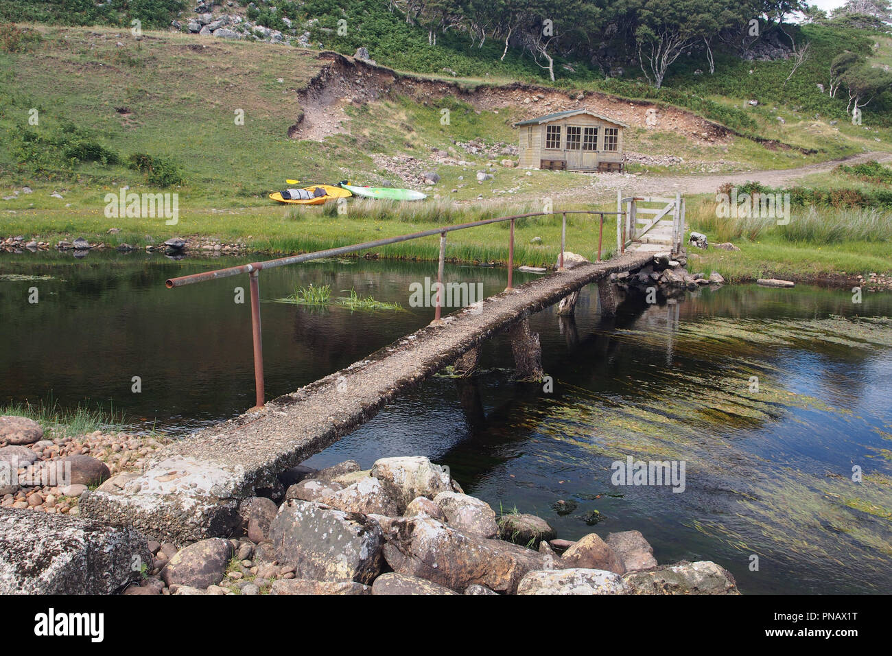 Ein Blick auf einem Fluss mit zwei Kajaks Festlegung auf der Bank neben einem Gartenhaus und einem schmalen Steg überspannt den Fluss und mit dem Fluss Stockfoto