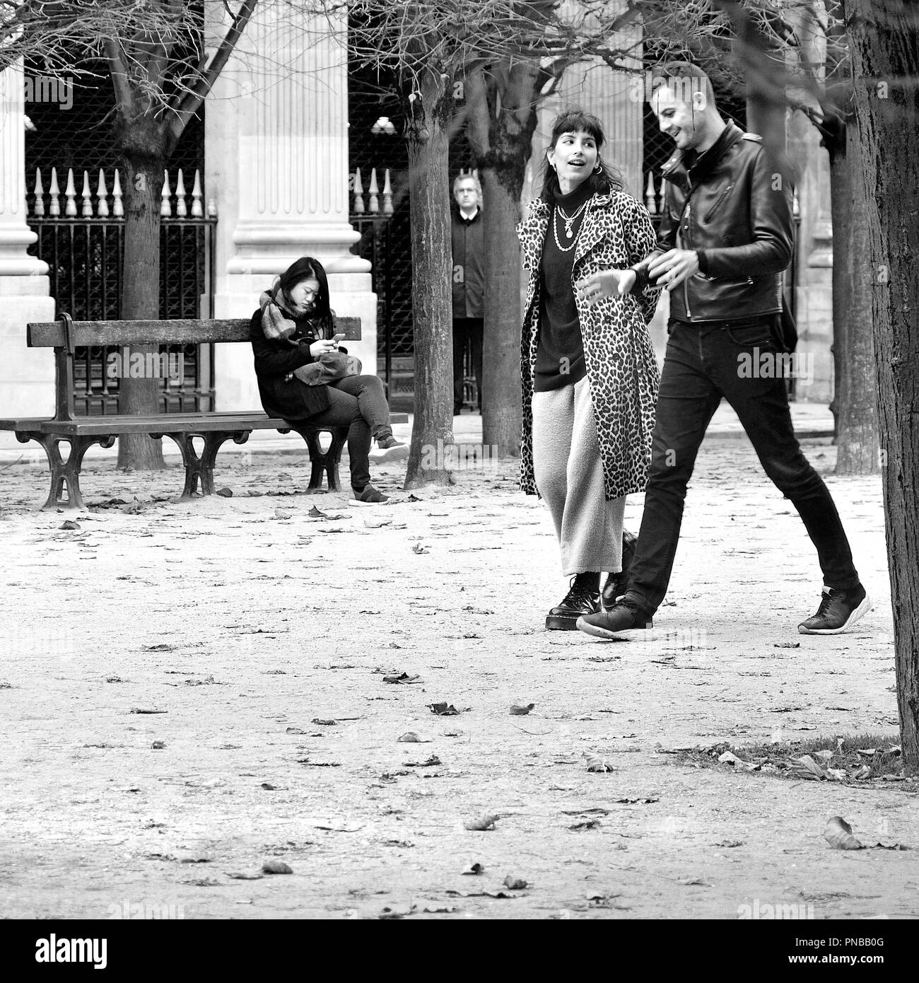 Paris, Frankreich. Palais Royal. Herbst, Frau entspannend auf einer Bank, junges Paar vorbei (und einem unheimlichen Mann zwischen den Bäumen). Stockfoto