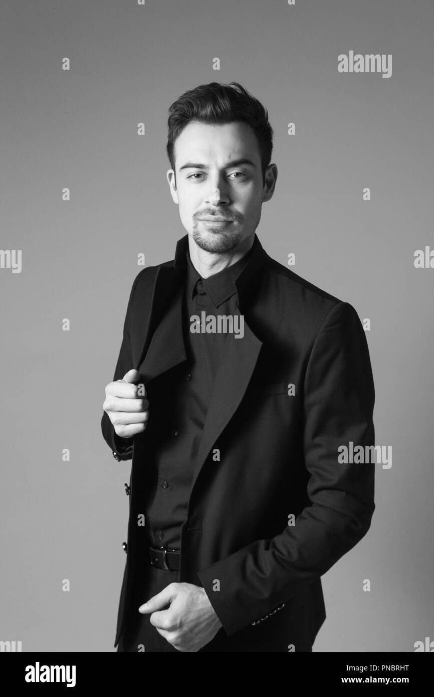 Jungen gutaussehenden Mann in einem schwarzen Anzug, stehend und ernst in die Kamera, gegen normales studio Hintergrund Stockfoto