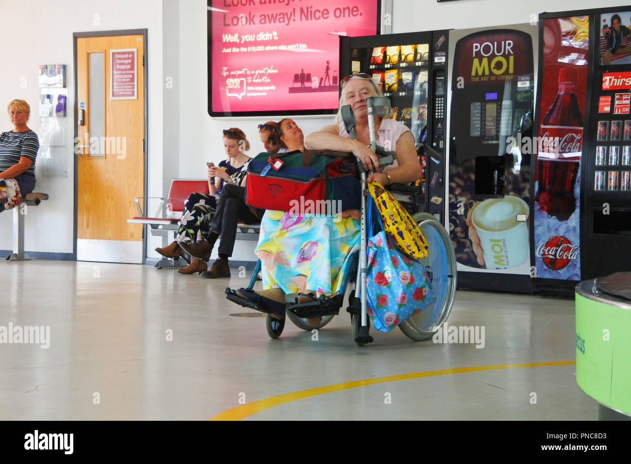 Ältere behinderte Frau in einem Rollstuhl warten auf ihr Gepäck am Flughafen Exeter, Devon, England - John Gollop Stockfoto