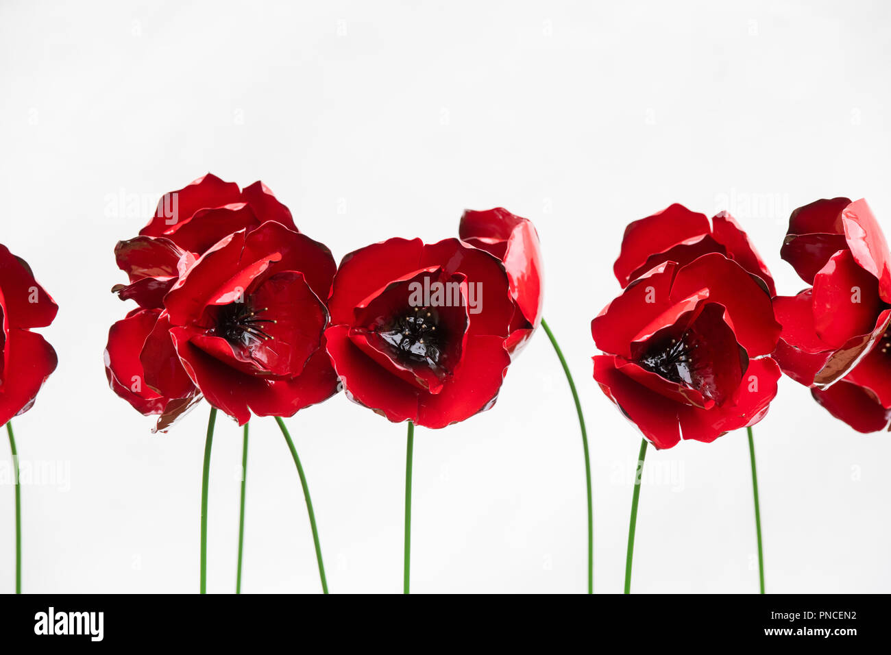 Linie der roten Metall geformt Mohn gegen eine weiße Wand an der RHS Wisley Flower Show 2018. RHS Wisley Gardens, Surrey, Großbritannien Stockfoto