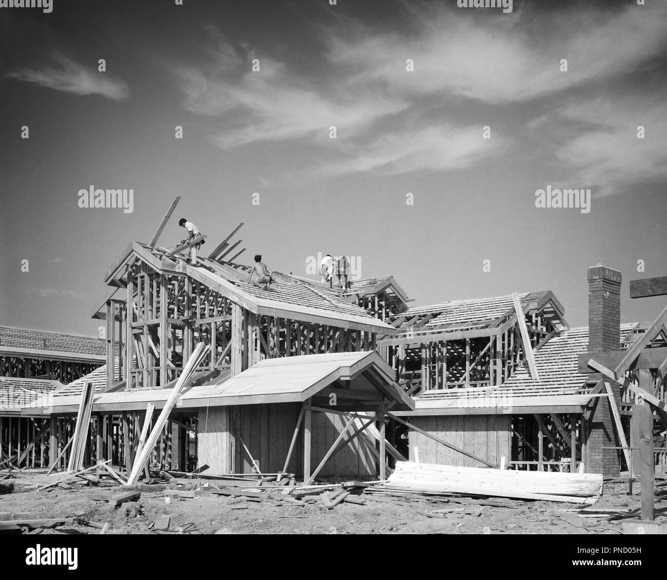 1970 s CREW VON VIER MÄNNERN ZIMMERLEUTE KONSTRUIEREN VON GROSSEN HOLZ BALLOON FRAME STICK gebautes Haus-b 26046 HAR 001 HARS WOHN- MÄNNER GEBÄUDE BUILDER B&W ZIELE WEITWINKEL SKILL BERUF STRUKTUR KOMPETENZEN ÄUSSERE WISSEN FORTSCHRITT WOHNUNGEN BERUFE UNVOLLENDETE FRAMING ZIMMERLEUTE RESIDENCE SPERRHOLZ HANDWERK GEBAUT BAUEN ZUSAMMENARBEIT BAUHOLZ Mitte - Mitte - erwachsener Mann zwei Geschichte junger erwachsener Mann SCHWARZ UND WEISS HAR 001 ALTMODISCH Stockfoto