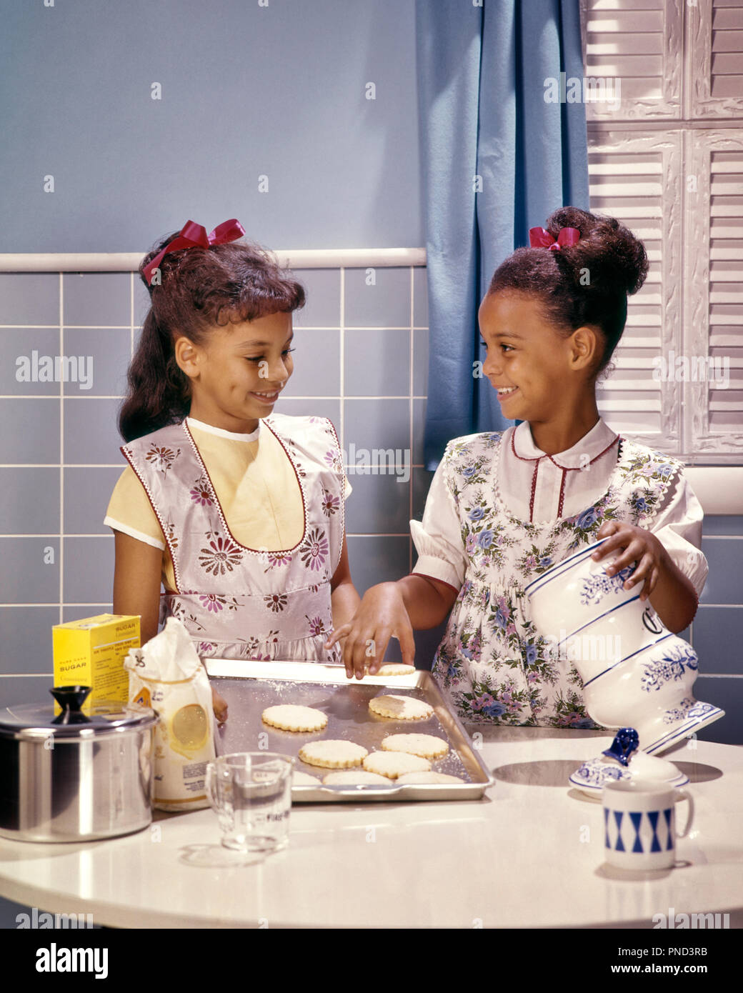 1960 s zwei lächelnde afrikanische amerikanische Mädchen Schwestern in der Küche backen Kekse - KJ 5134 PHT 001 HARS KOPIE RAUM MIT HALBER LÄNGE INSPIRATION COOKIES GESCHWISTER VERTRAUEN SCHWESTERN SCHÜRZEN ERFOLG GLÜCK WELLNESS afrikanische Amerikaner, AFRICAN-AMERICAN AUFREGUNG WISSEN FREIZEIT AFRIKANISCHE ETHNIE GESCHWISTER LÄCHELT BÄCKER SCHWARZE KÖCHE HAARBÄNDER FREUDIGE STILVOLLE ZUSAMMENARBEIT HAARBAND JUGENDLICHE KÜCHEN ZWEISAMKEIT ALTMODISCHE afrikanische Amerikaner Stockfoto