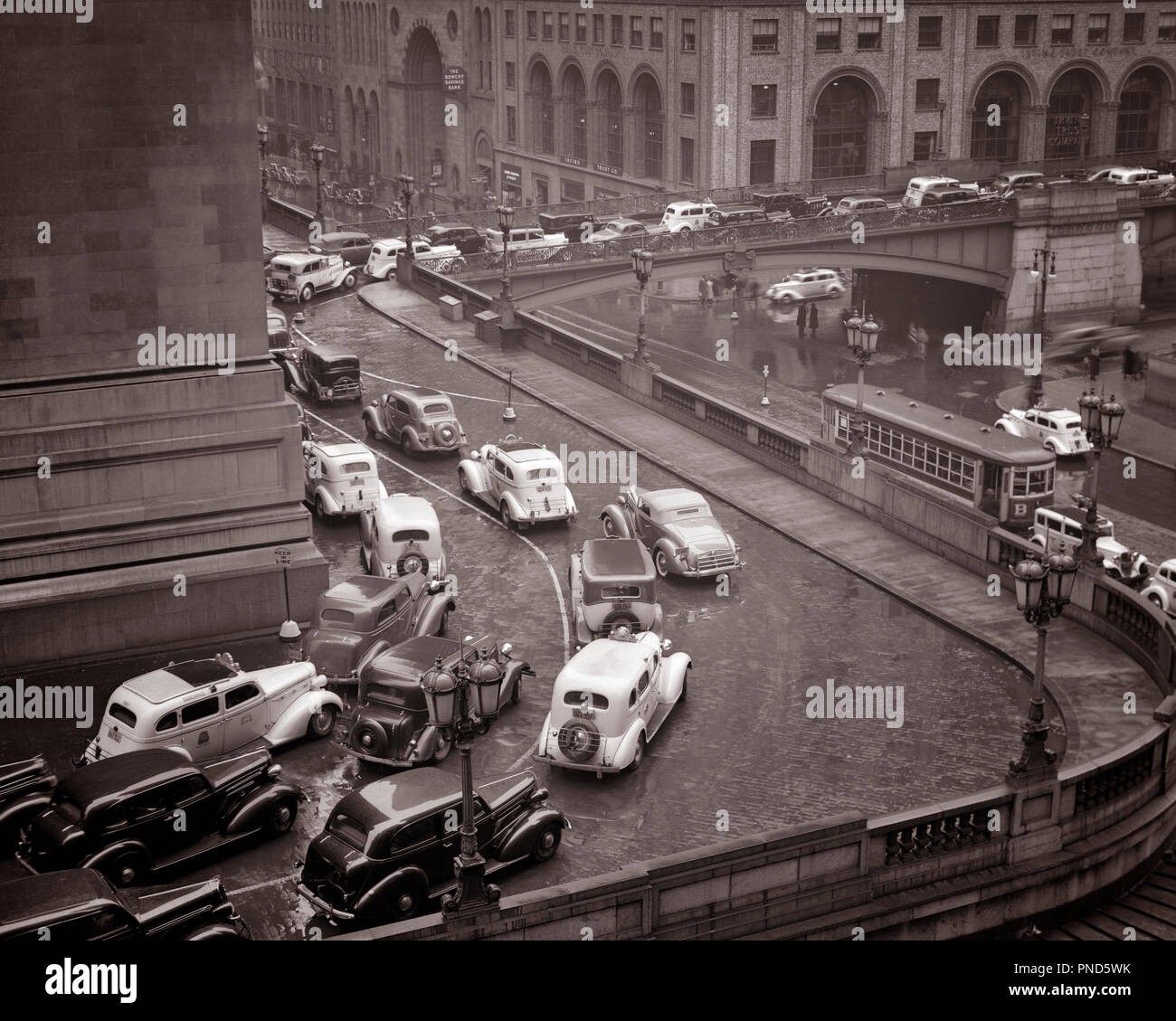 1930er Jahre regnerischen Tag STAU RUND UM DIE GRAND CENTRAL STATION, Pershing Square und 42ND STREET MIDTOWN MANHATTAN EASTSIDE NEW YORK USA-q 37701 CPC 001 HARS UND AUTOS ÄUSSERE FORTSCHRITT RICHTUNG NEW YORK GRAND CENTRAL BEWEGUNGSUNSCHÄRFE KONZEPTIONELLE NEW YORK AUTOMOBILE STÄDTE FAHRZEUGE EASTSIDE NEW YORK CITY RUNDUNG PERSHING SQUARE STAUS TAXIS 42ND STREET schwarze und weiße Taxis ALTMODISCHE ÜBERFÜHRUNG STRASSE AUTO TROLLEY Stockfoto