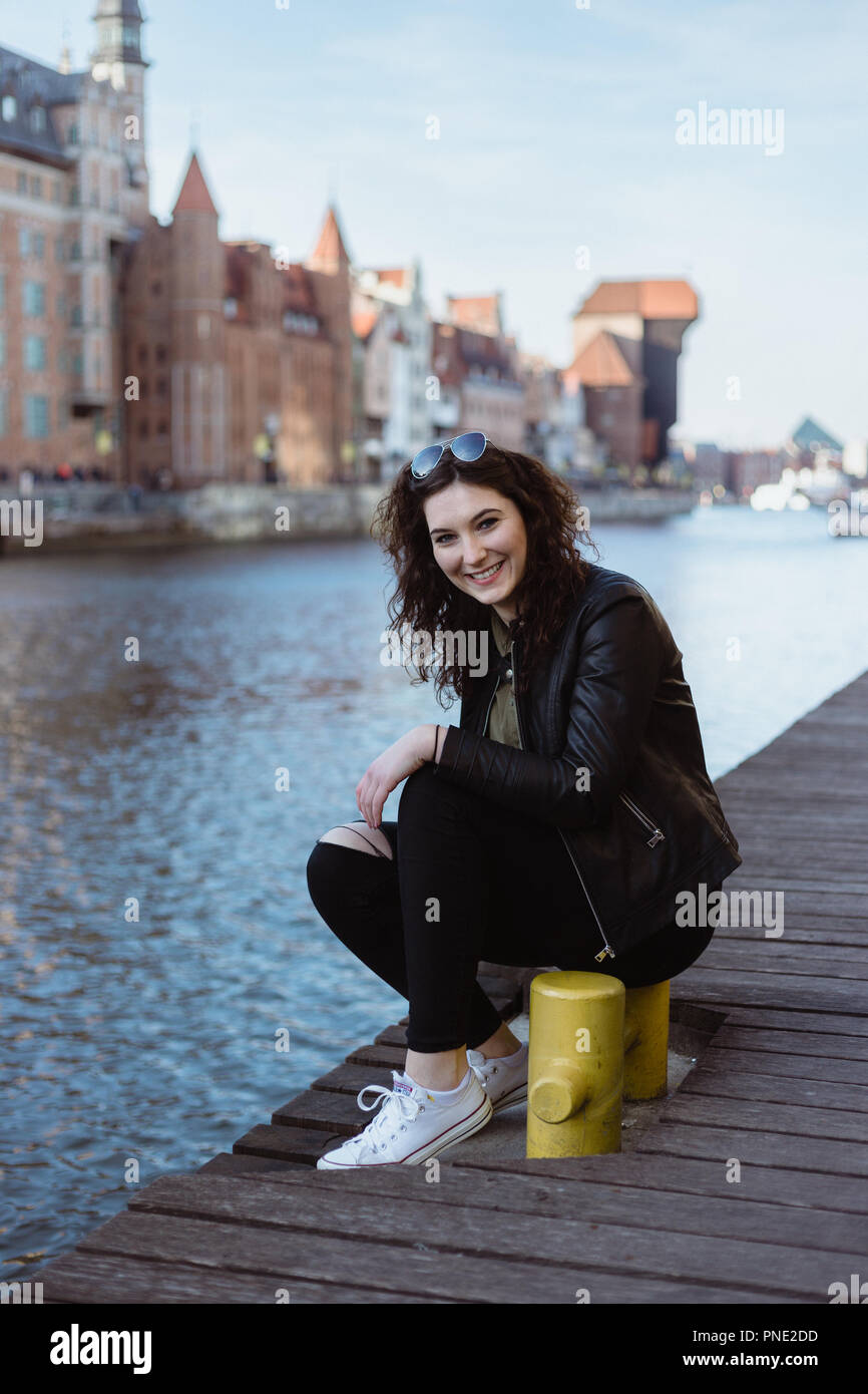 Junge Frau in eine Lederjacke gekleidet sitzt durch den Fluß Pier in Danzig, Polen, Lachen. Stockfoto