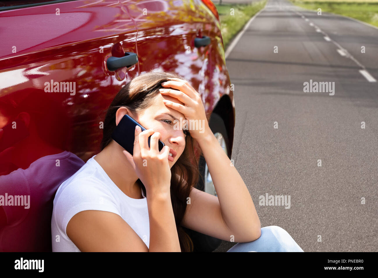 Betonte Frau auf der Suche nach Hilfe auf Handys nach Autopanne Stockfoto