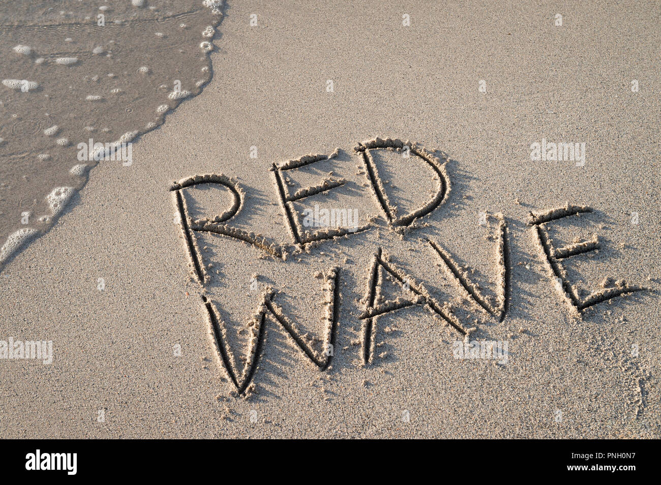 'ReD WELLE' in den Sand geschrieben am Strand mit Meerblick Waschmaschine bis zum Ufer. Stockfoto