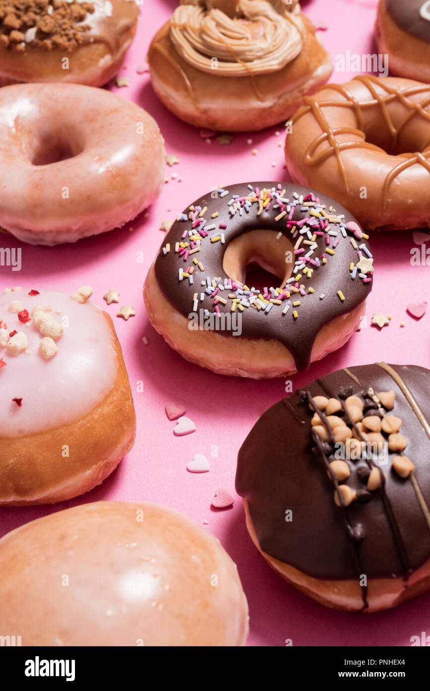 Sortierte Donuts auf einem rosa Hintergrund. Mit klassischen Schokolade besprüht Donut sowie Erdbeeren und Sahne mit verstreuten besprüht und Herz Stockfoto