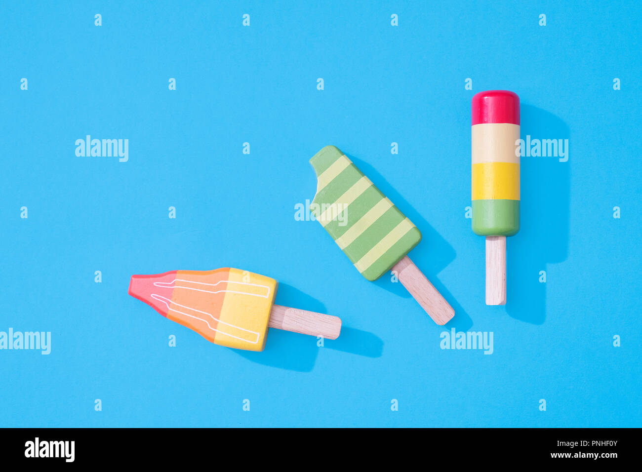 Drei Holzspielzeug eis Lutscher Eis am Stiel auf einem Pastell-blaue Hintergrund mit Platz für Text mit minimalistischen Zusammensetzung Stockfoto