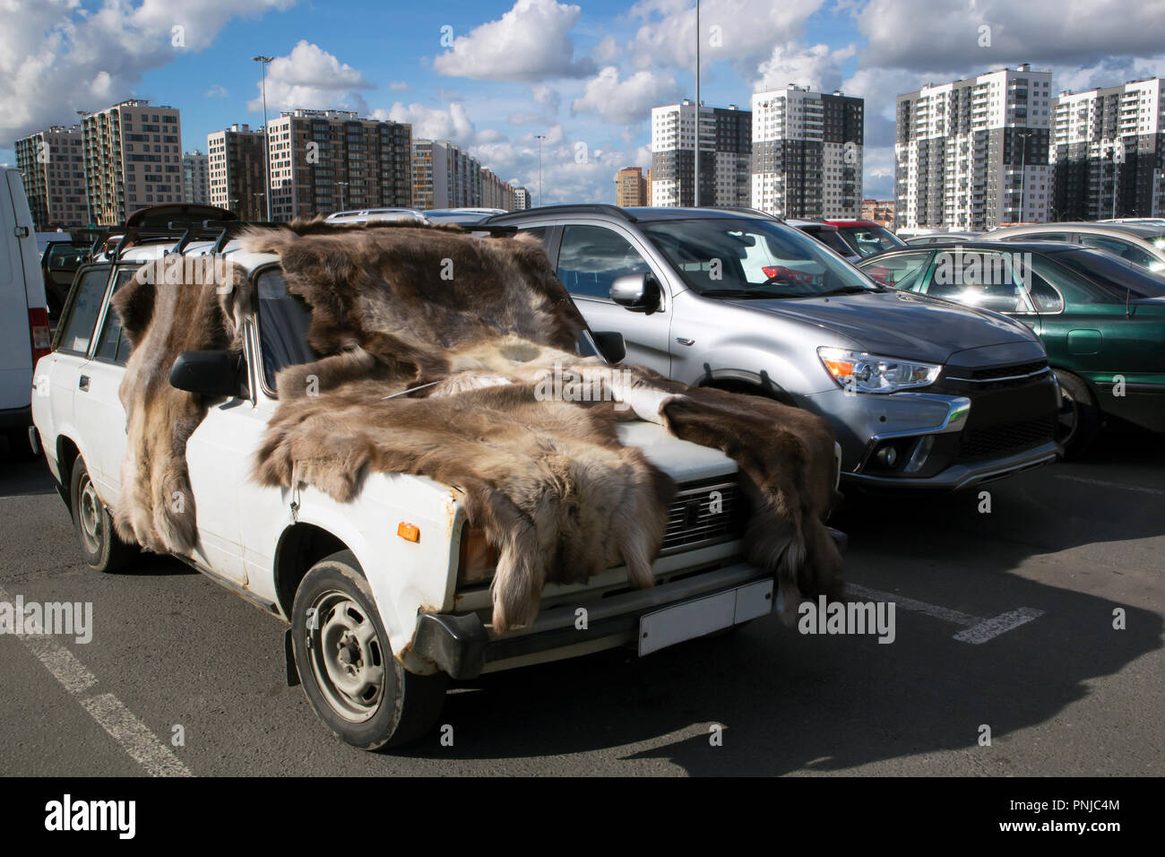 Alten rostigen Auto mit Fellen abgedeckt auf einem großen Parkplatz gegen moderne Stadtbild und Sky Stockfoto